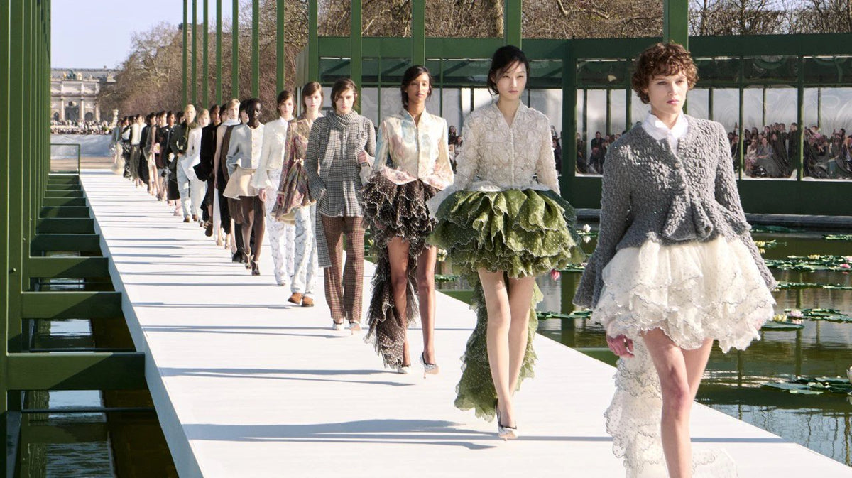 Models on a long white runway beside a lily pond in a glass pavilion in Paris