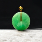 Green jade pendant with gold setting on a dark background