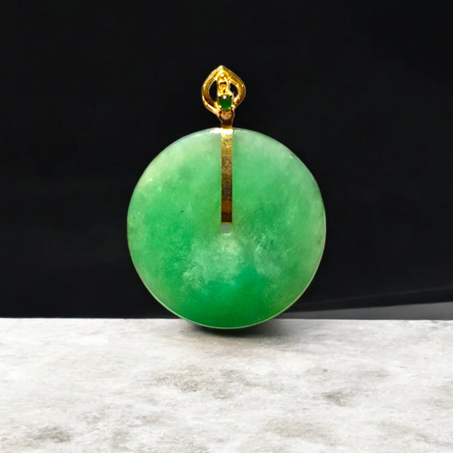 Green jade pendant with gold setting on a dark background