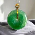Green jade pendant with gold accents on a gray fabric background