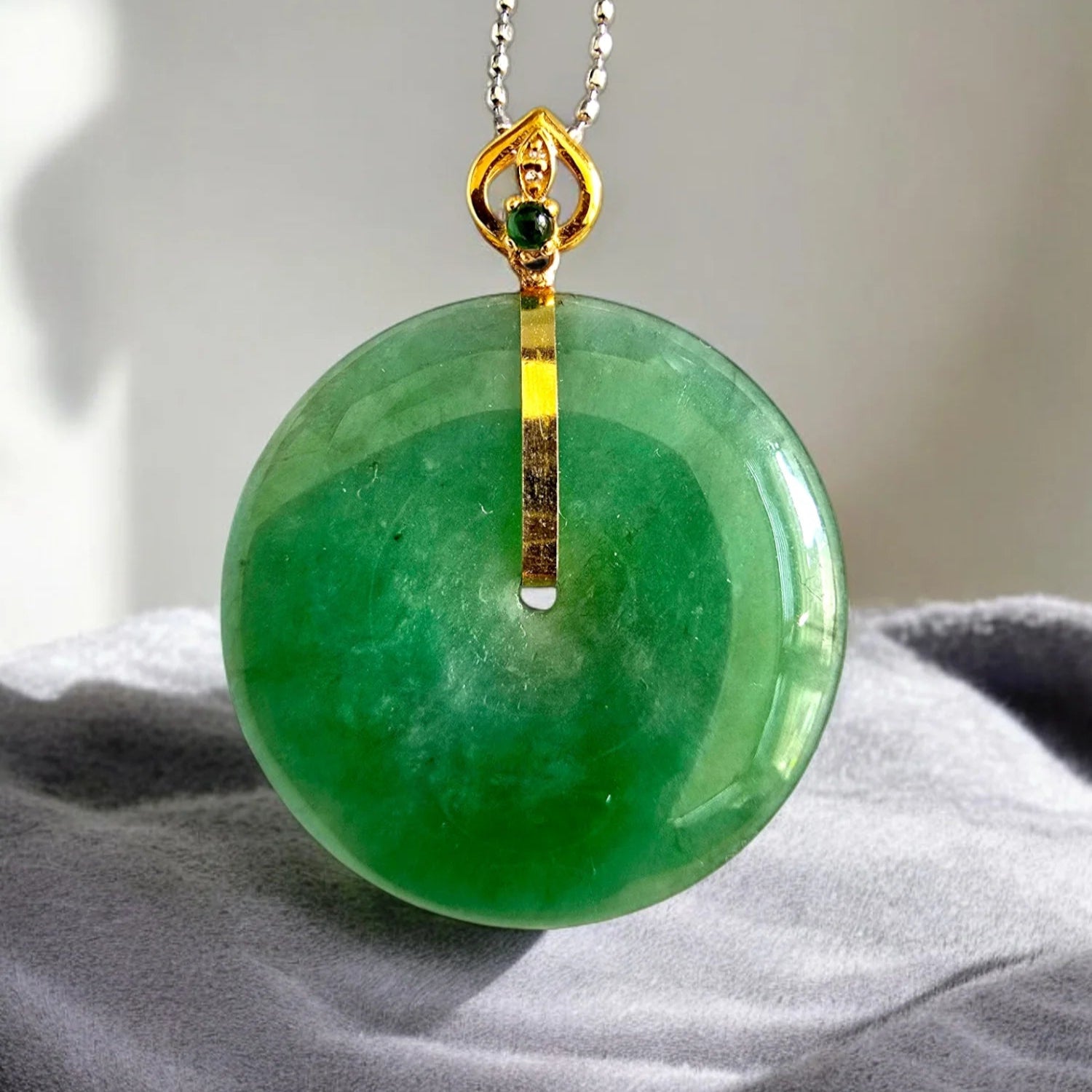 Green jade pendant with gold accents on a gray fabric background