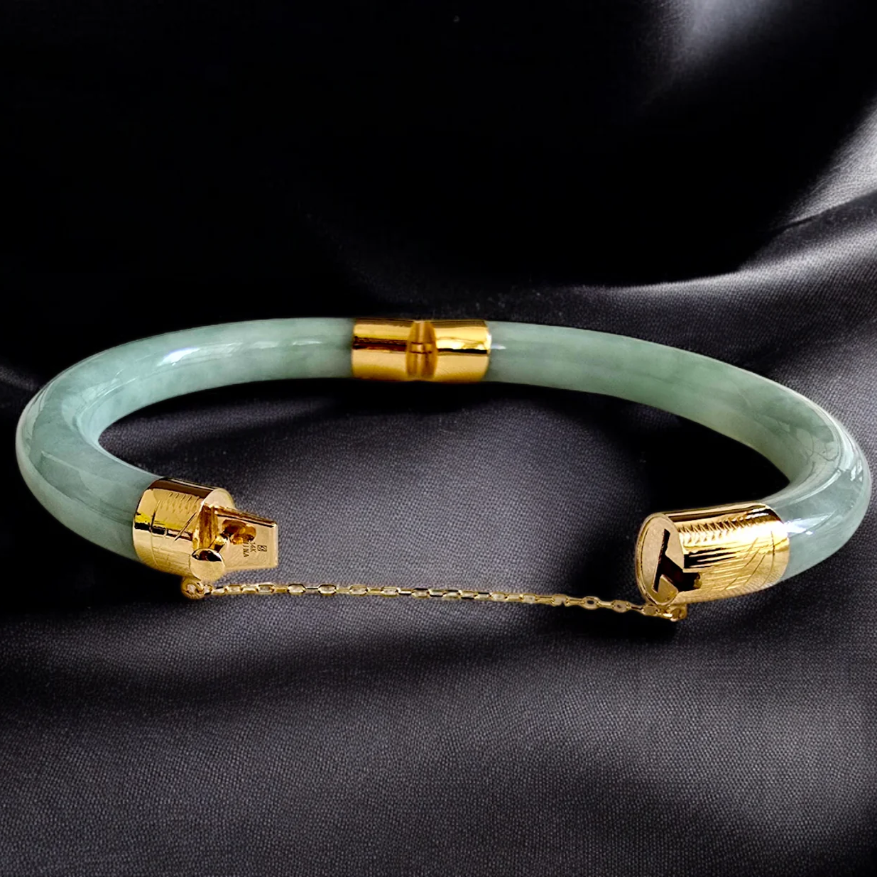 Green jade bracelet with gold accents on a black satin background