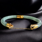 Green jade bracelet with gold accents on a black satin background