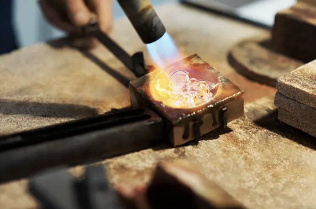 A goldsmith heating gold with a torch at the workbench