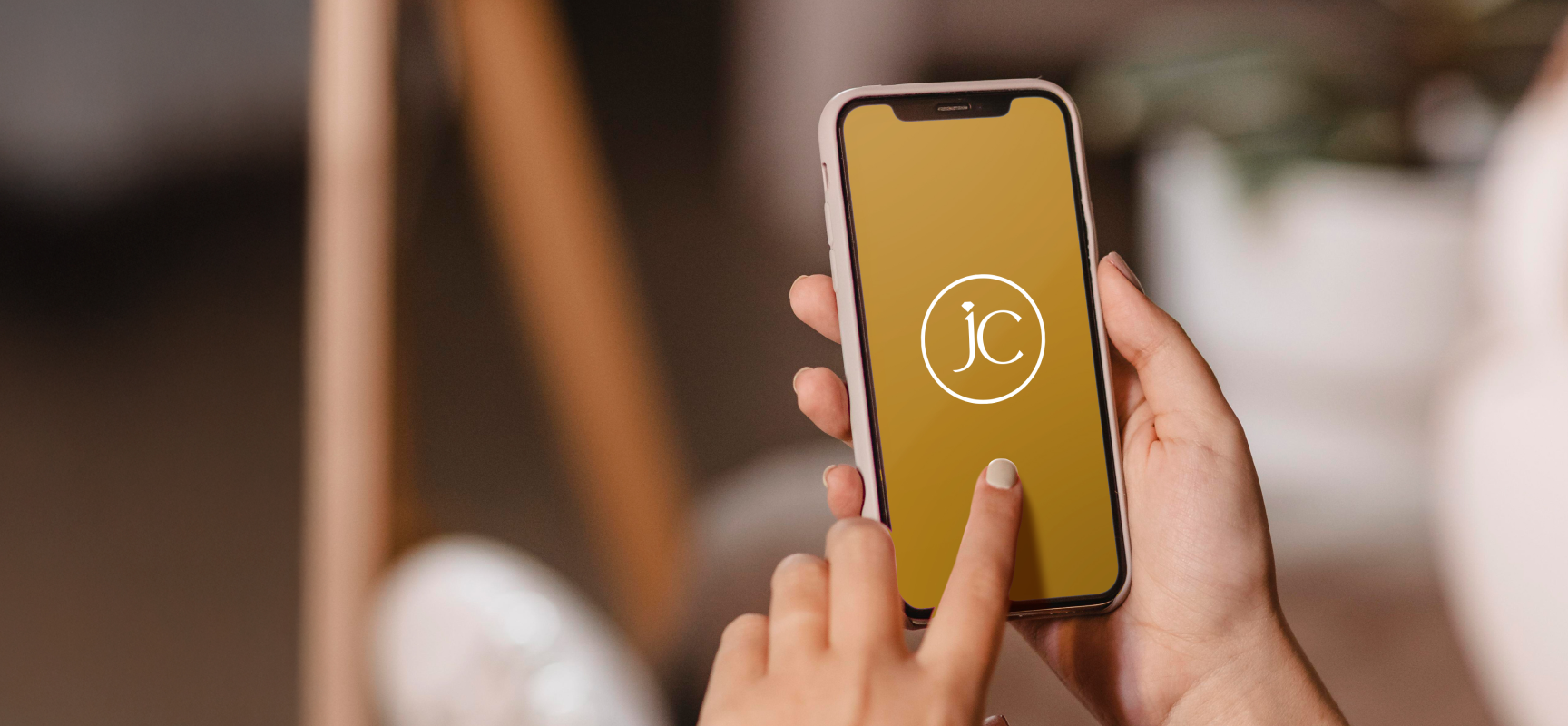 Hands holding phone showing gold JC monogram app screen