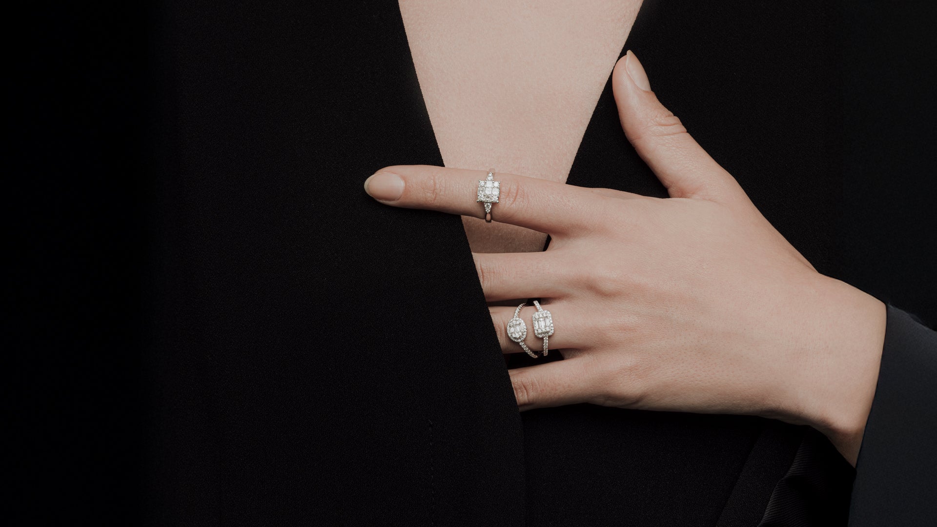 Hand with emerald-cut diamond rings against black outfit